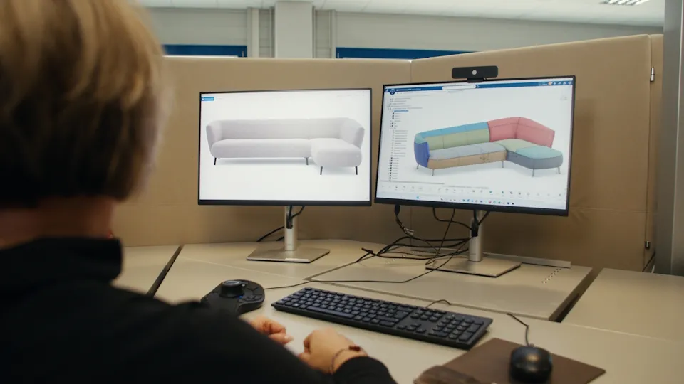Rolf Benz designer using the 3DEXPERIENCE platform on dual monitors to configure a custom sofa in 3D.