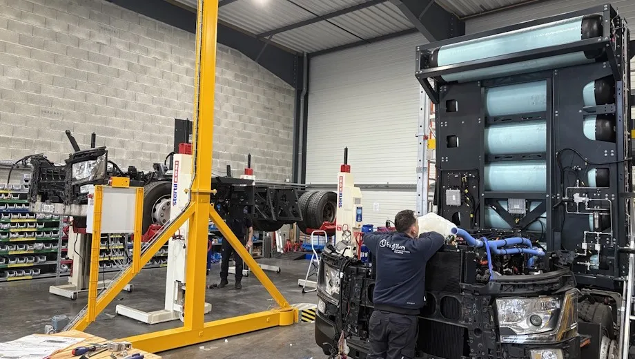 Technician retrofitting a hydrogen powertrain on a heavy-duty truck inside a Hyliko workshop, with hydrogen tanks visible.